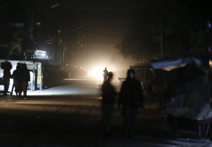 People are silhouetted on vehicle's headlights on a dark street during widespread power outages in Rawalpindi, Pakistan, Sunday, Jan. 10, 2021. Pakistan's national power grid experienced a major breakdown late night on Saturday, leaving millions of people in darkness, local media reported. (AP Photo/Anjum Naveed)