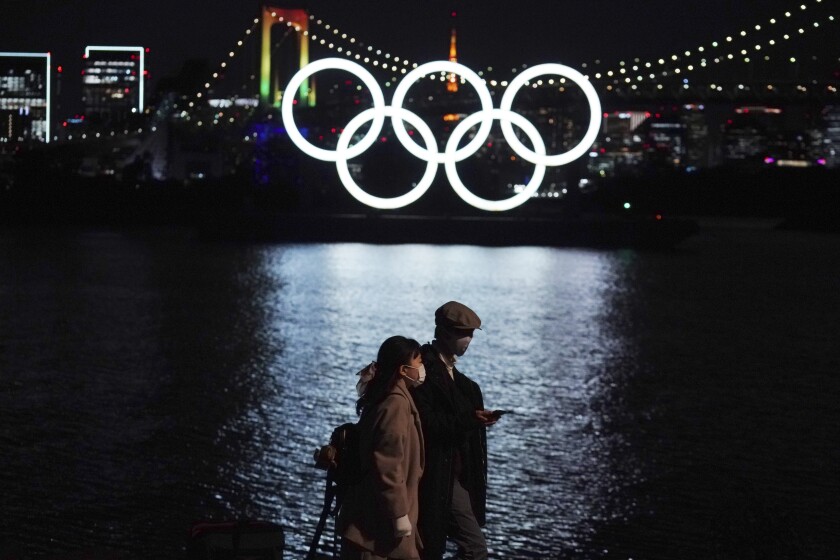 FILE - In this Dec. 1, 2020, file photo, a man and a woman walk past near the Olympic rings floating in the water in the Odaiba section in Tokyo. More than 80% of people in Japan who were surveyed in two polls in the last few days say the Tokyo Olympics should be canceled or postponed, or say they believe the Olympics will not take place. (AP Photo/Eugene Hoshiko, File)