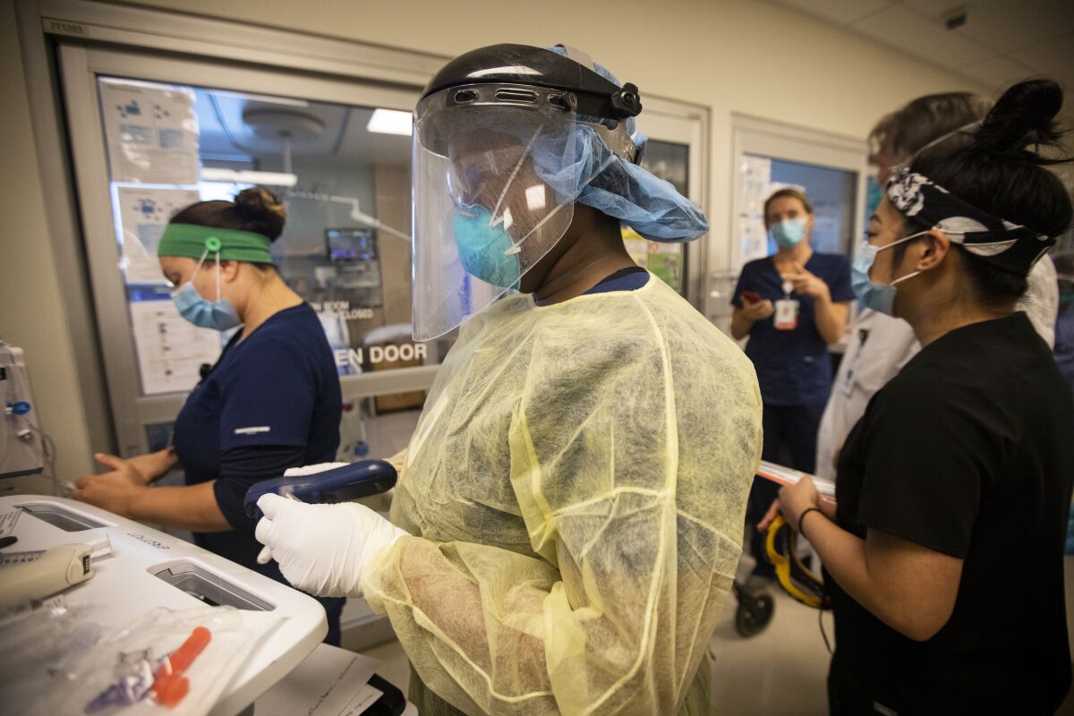 A nurse in full protective gear in a hospital hallway with other healthcare workers in masks