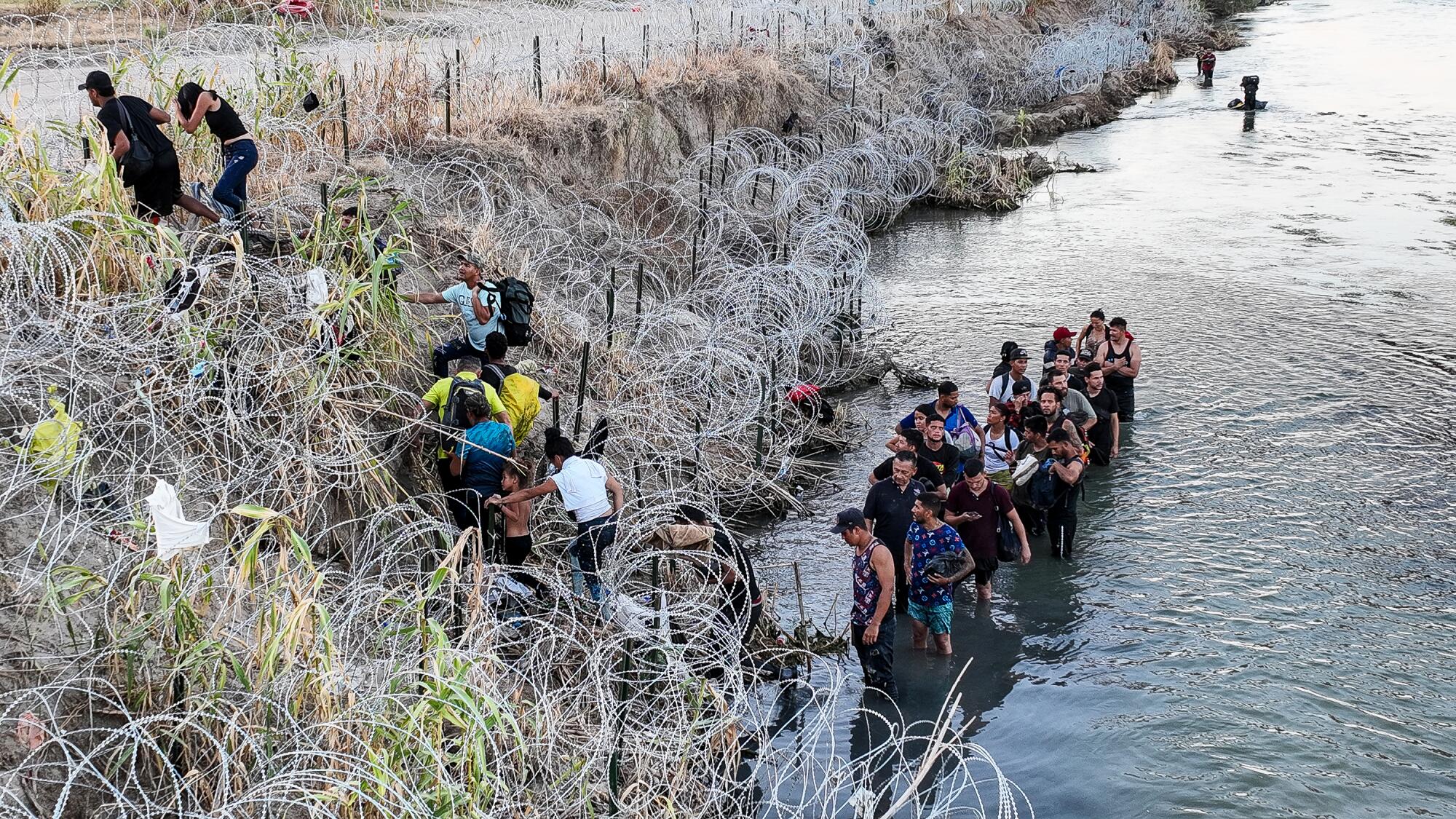 People standing in a river and on a river bank try to find a way through razor wire on the river bank.