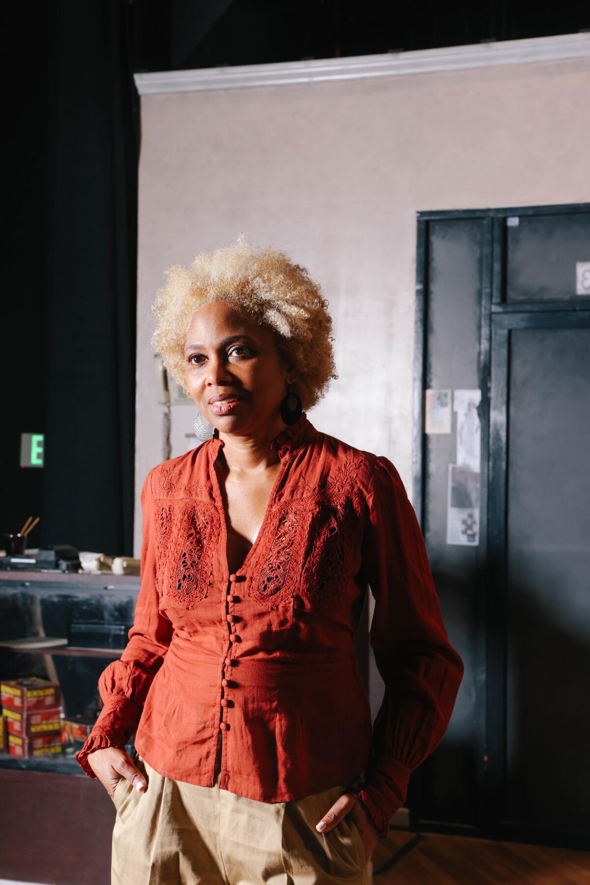 A woman in a dark orange top stands near the stage at a theater. 