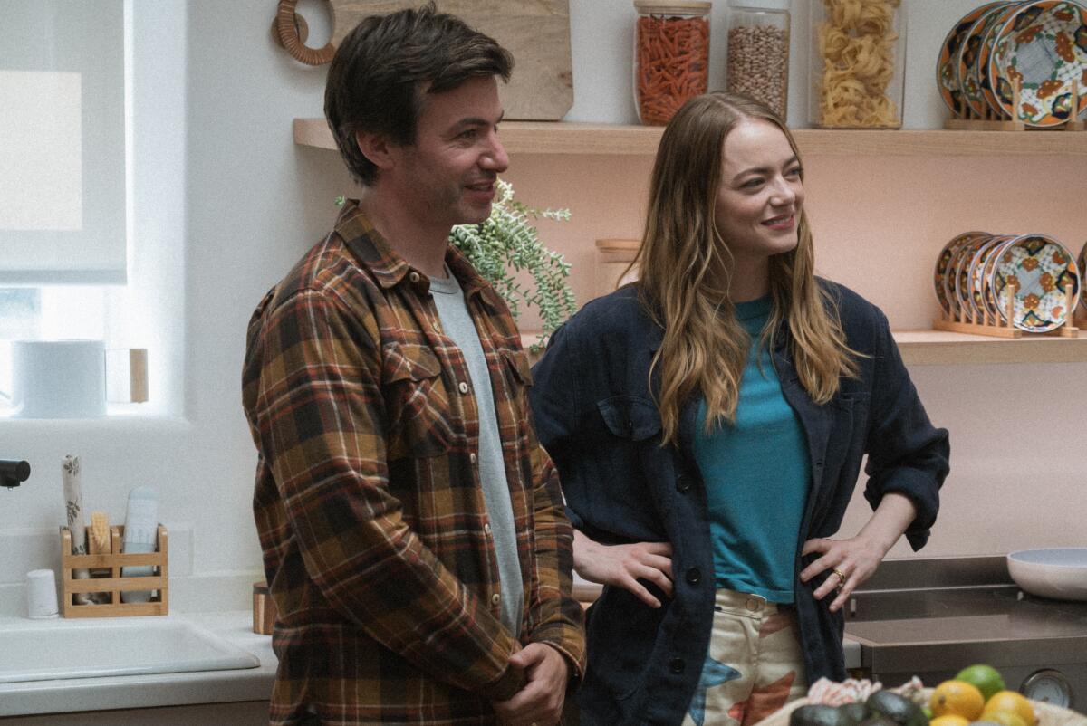 Asher, in a flannel shirt and gray T-shirt, stands next to Whitney in a kitchen.