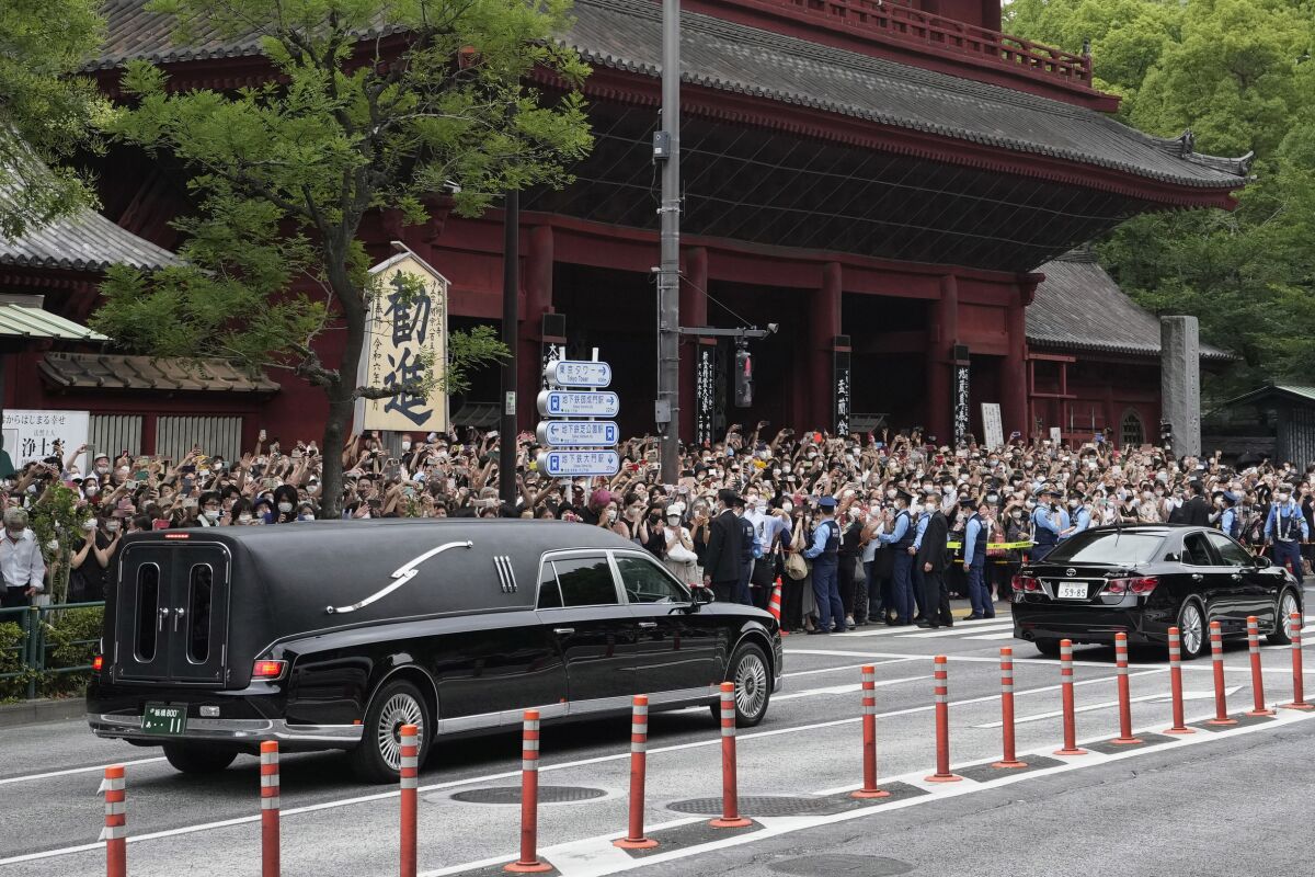 A hearse with Shinzo Abe's body drives past a crowd outside a temple.