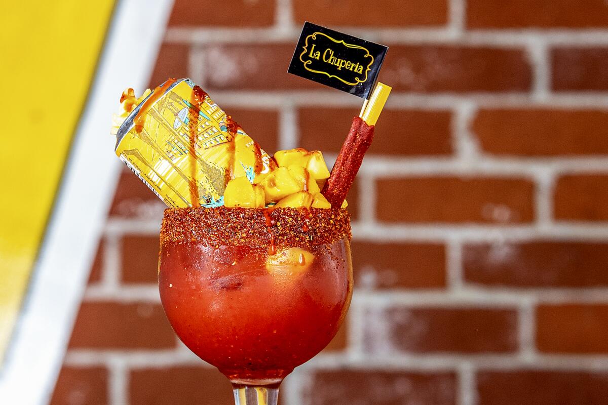 A michelada in a glass goblet with upside-down Pacifico bottle in it, a mango garnish and swirls of red spice.