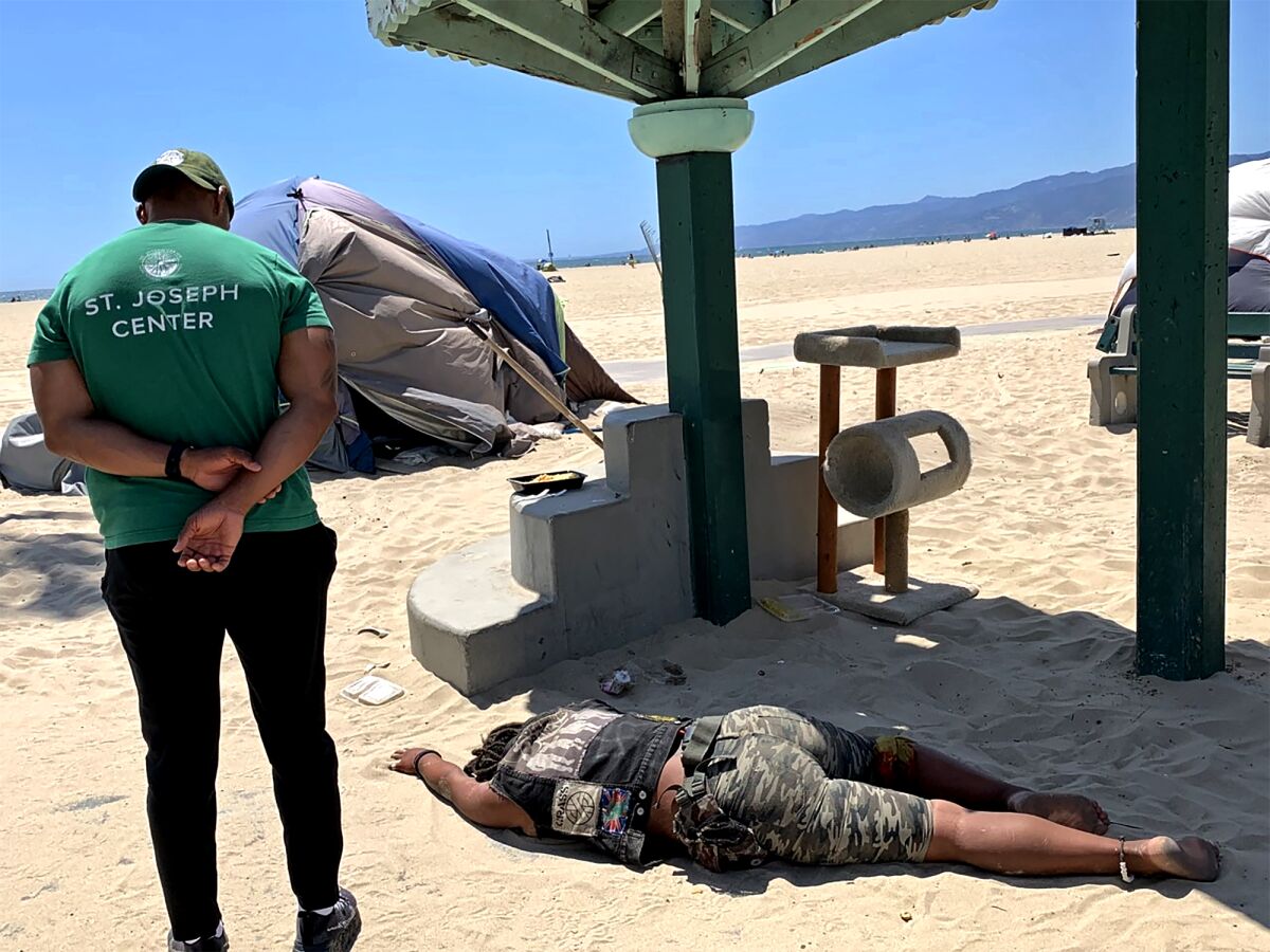 An outreach worker checks on an unhoused woman lying on Venice Beach on June 23, 2021. 