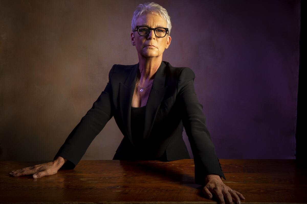 A woman with short silver hair and glasses leans on a table.