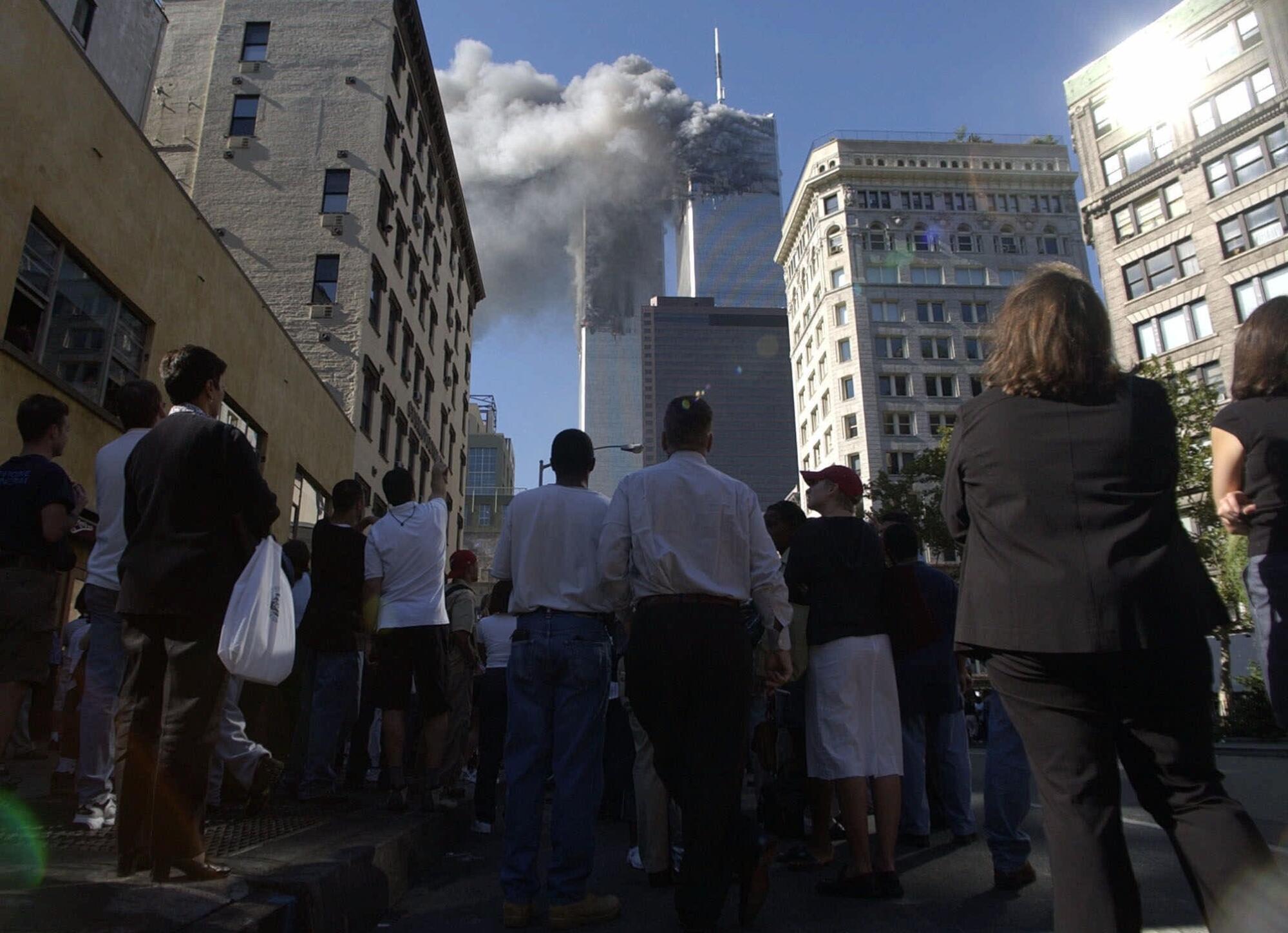 People gather in a street watching smoke pouring from the twin towers. 