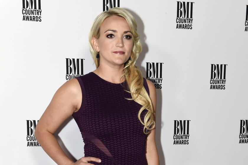 A woman with long blond hair poses with her right hand on her hip