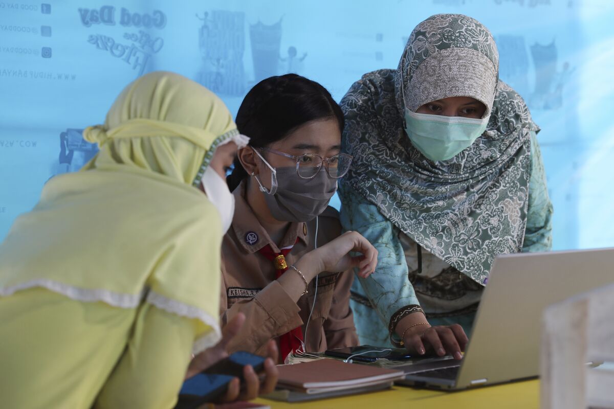 A mother, right, and her daughter, center, wear face masks to help curb the spread of the new coronavirus as they use free wifi to access an online lesson inside a temporary tent in Jakarta, Indonesia, Wednesday, Aug. 12, 2020. In some areas of the country, students are still yet to go to school due to the coronavirus. (AP Photo/Achmad Ibrahim)