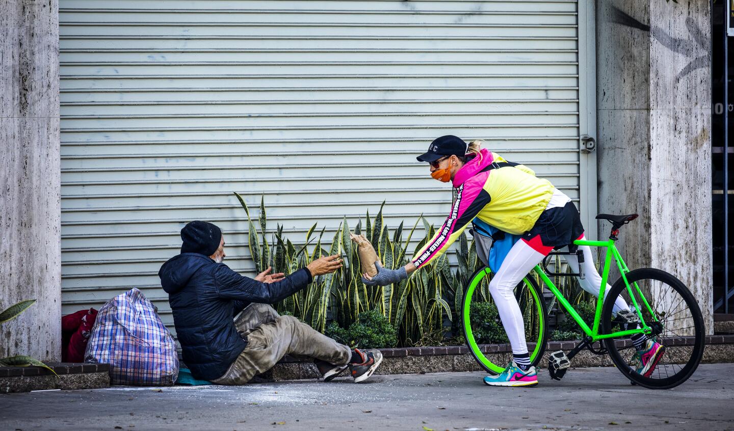 Bicycle Meals volunteer Alex Gilbertson delivers a bagged meal to a homeless man on Wilshire Boulevard in Koreatown.