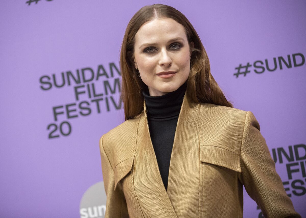 A woman in a jacket and turtleneck poses upon arrival at a movie premiere