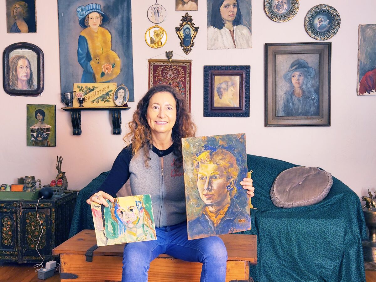 With a portrait she painted in one hand and an older art piece in the other, Sheree Perelman sits on an antique trunk.