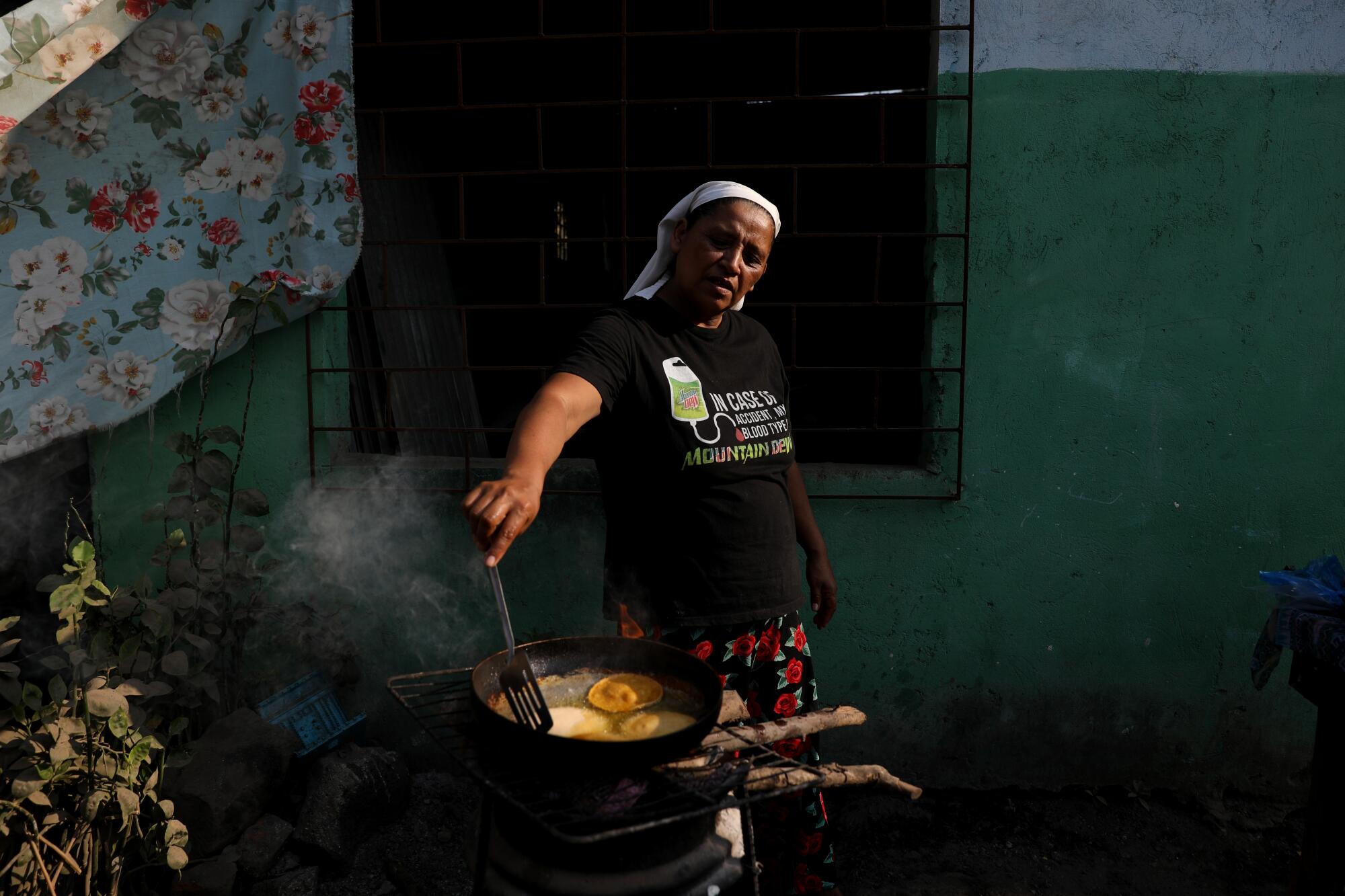A woman prepares enchiladas over an outdoor stove