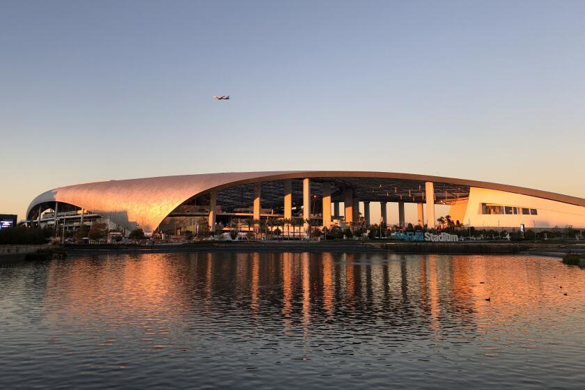 SoFi Stadium's gently curving roof seem to curl into the water of the lake in Lake Park