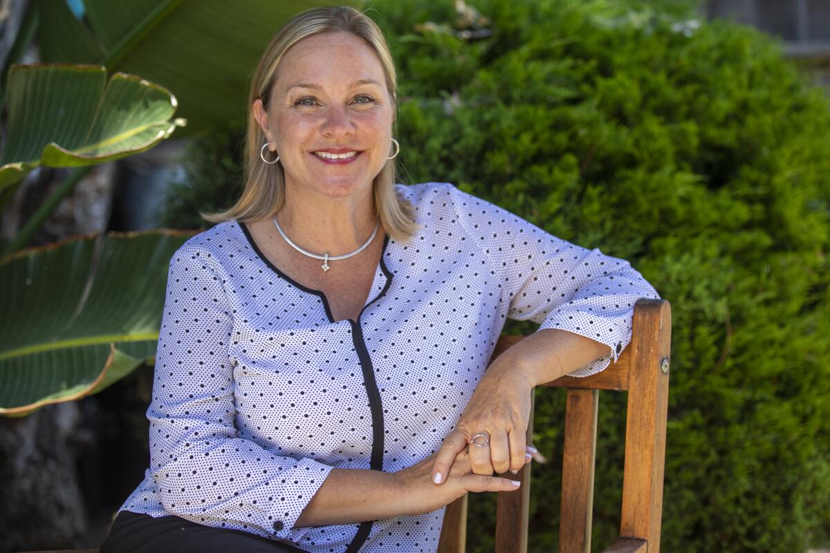 A woman sits in a chair in front of foliage