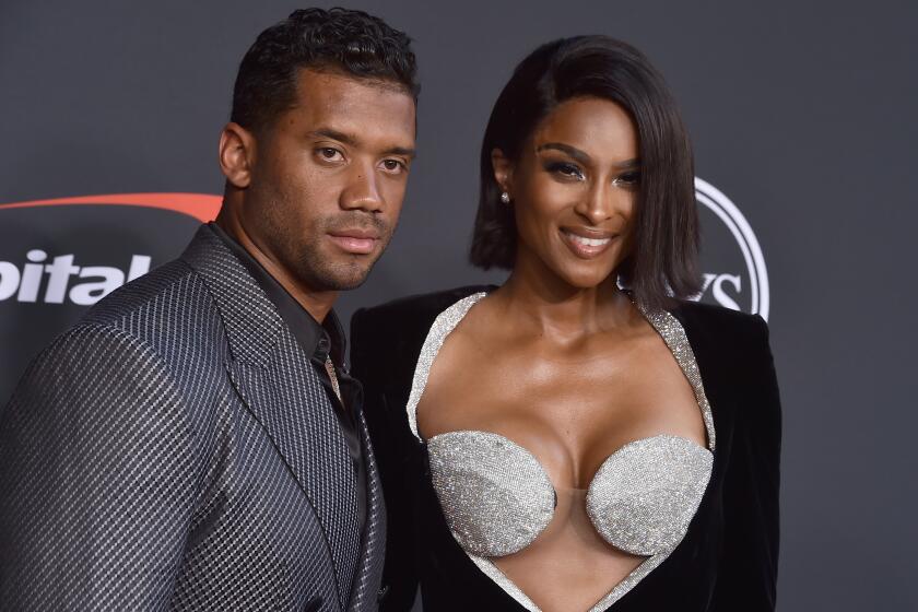 Russell Wilson posing in a patterned suit with Ciara posing in a sparkly bra and black jacket.