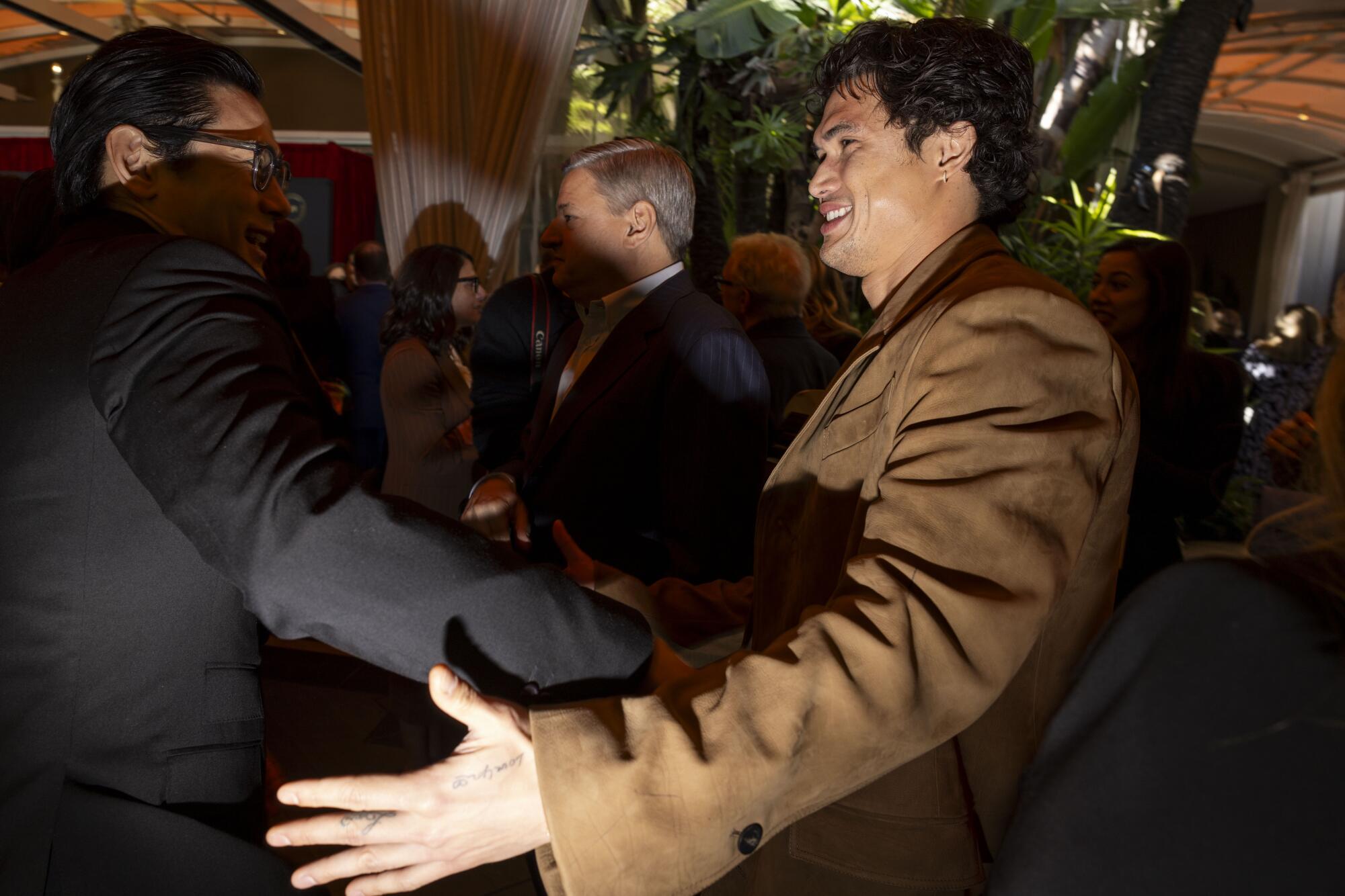 A man in a brown jacket is greeted by a man in a black jacket at a party.