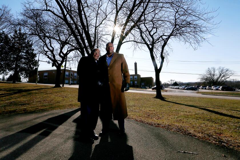 Jerome Greer, left, and his son Jason stand in Flora Park, where cross burnings greeted his arrival in the early 1990s as the first black school principal in Dubuque, Iowa. Greer worked at Irving Elementary School, seen in background.