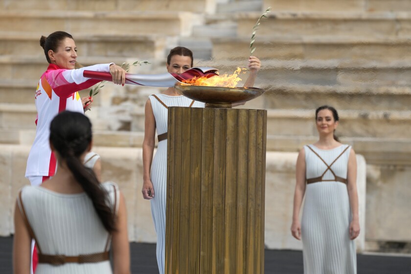 La campeona griega de esquí Paraskevi Ladopoulou (izquierda) enciende la antorcha durante la ceremonia de entrega de la llama olímpica, en el estadio Panathinean, en Atenas, Grecia, el 19 de octubre de 2021. (AP Foto/Thanassis Stavrakis)