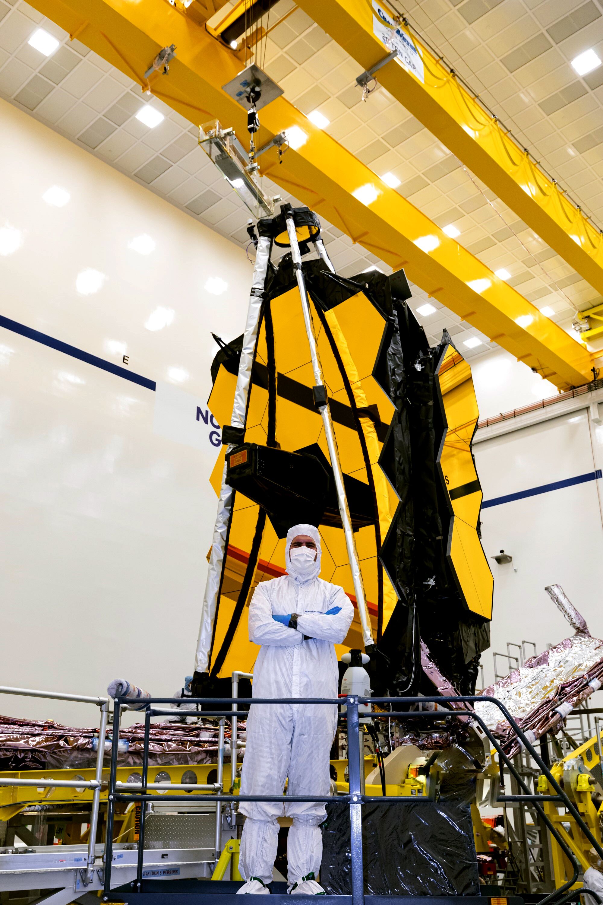 A man in a sanitary white suit stands before the folded-up telescope