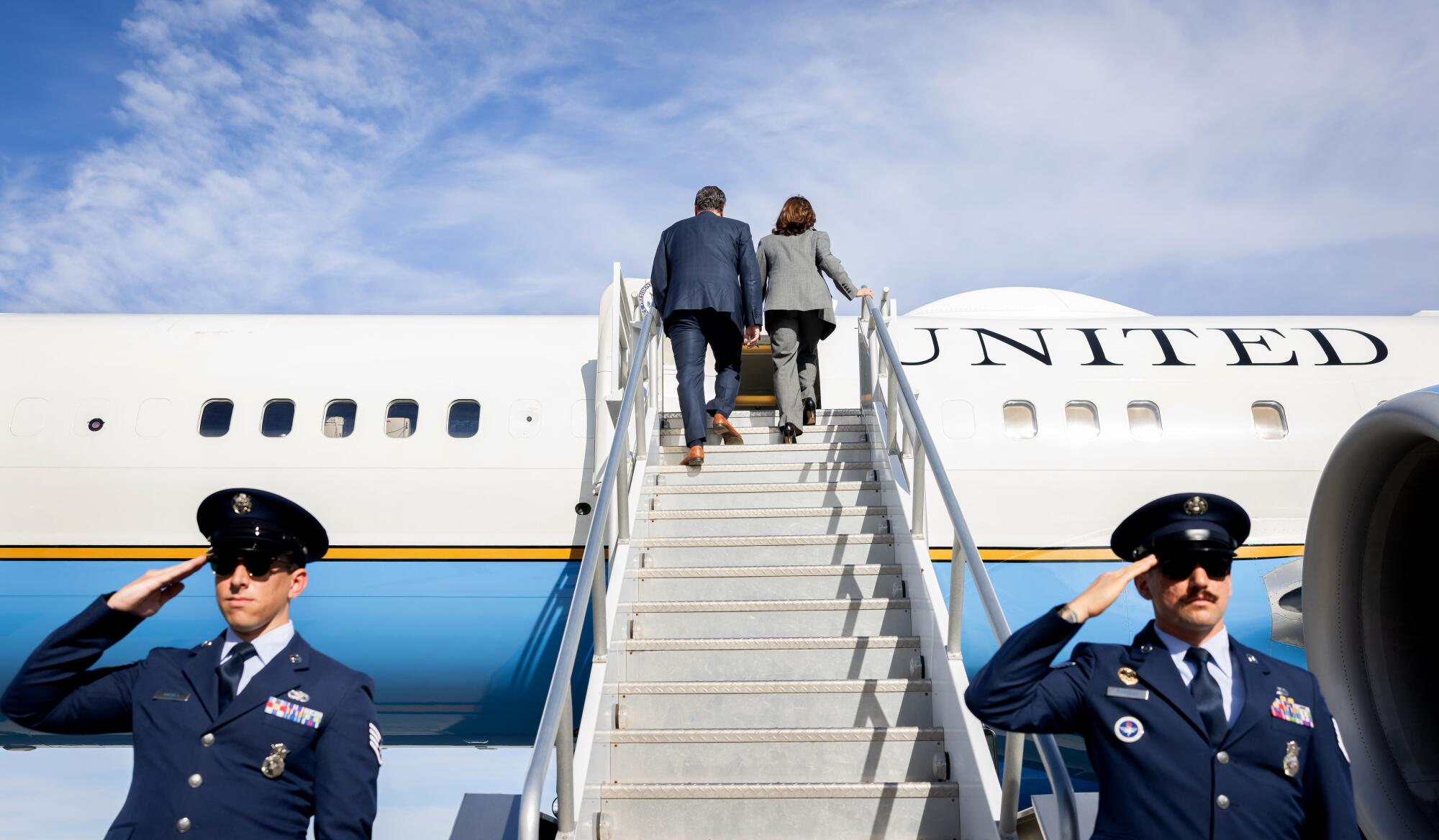 Vice President Kamala Harris and Second Gentleman Doug Emhoff board Air Force Two as two military members salute.