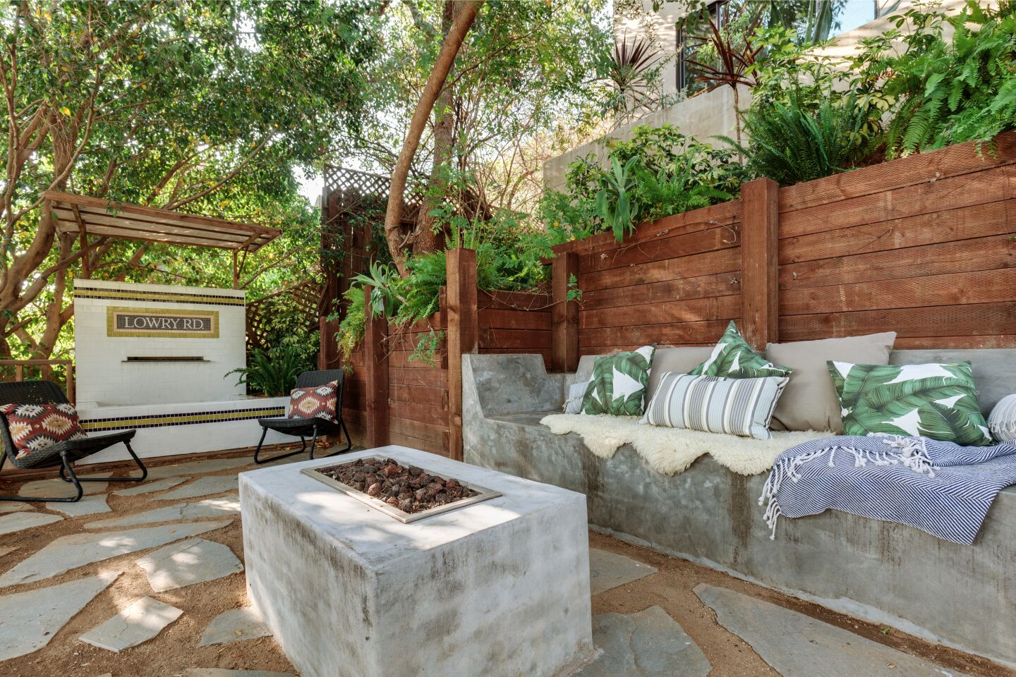 The fire pit with a sitting area nearby and greenery behind a retaining wall.