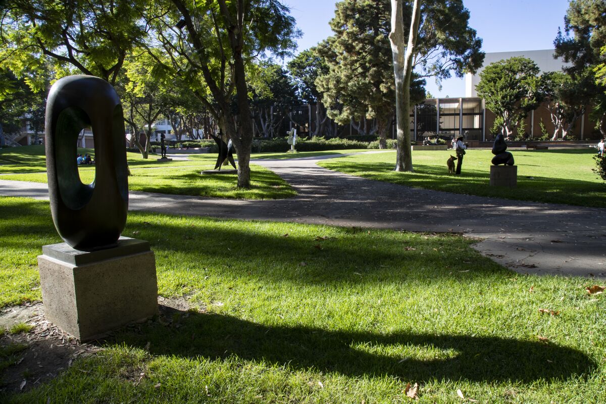 In the foreground of a grassy area with paths and trees is an oblong-shaped sculpture with a hole in the center.