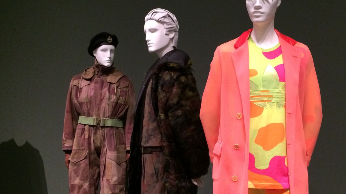 In a section devoted to military inspired-fashion, mannequins show a 20th century evolution of the style — including an English army tank suit from the 1940s, left, a camouflage ensemble by Jean Paul-Gaultier from his 2011-12 fall-winter collection, center, and a sportier 2013-14 outfit by Jeremy Scott.