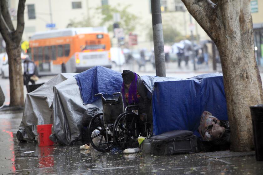 A woman crawls out of her tent and gets into her wheelchair on skid row outside the Union Rescue Mission.