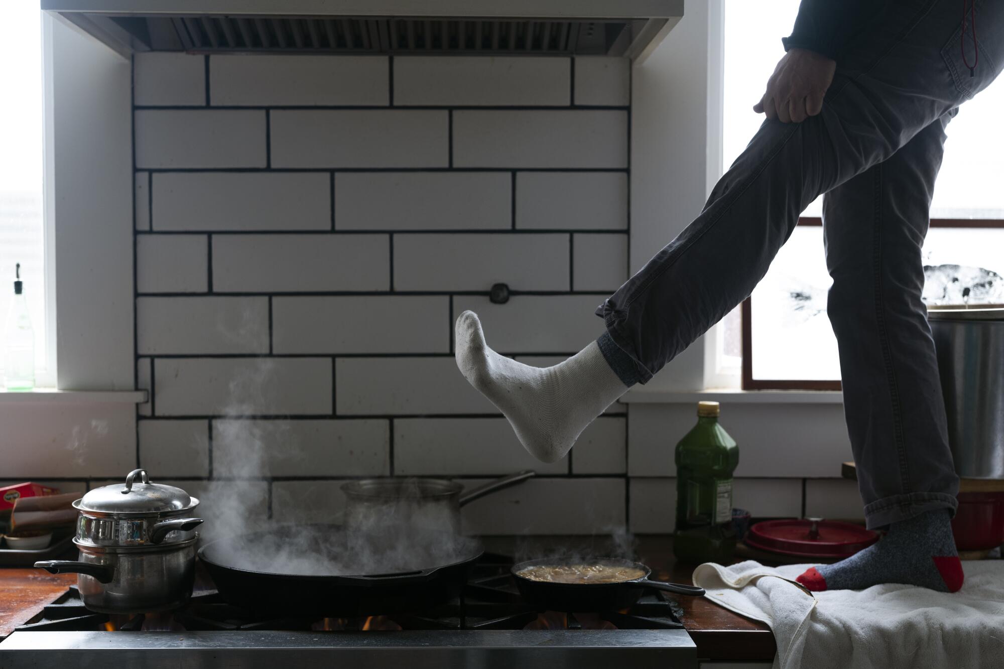 A man warms his foot over a stove. 