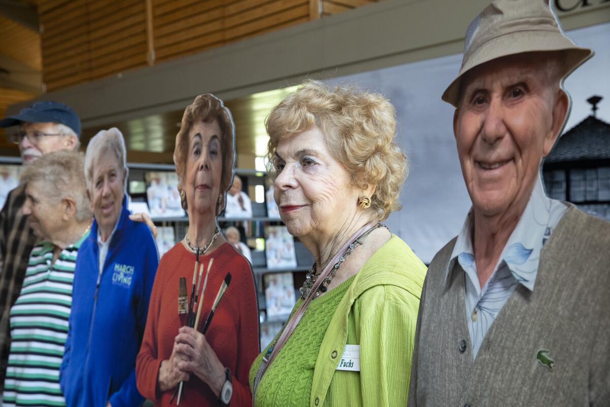 Anita Fuchs stands next to a cardboard cutout of herself at a Holocaust remembrance exhibit at Rancho San Diego Library
