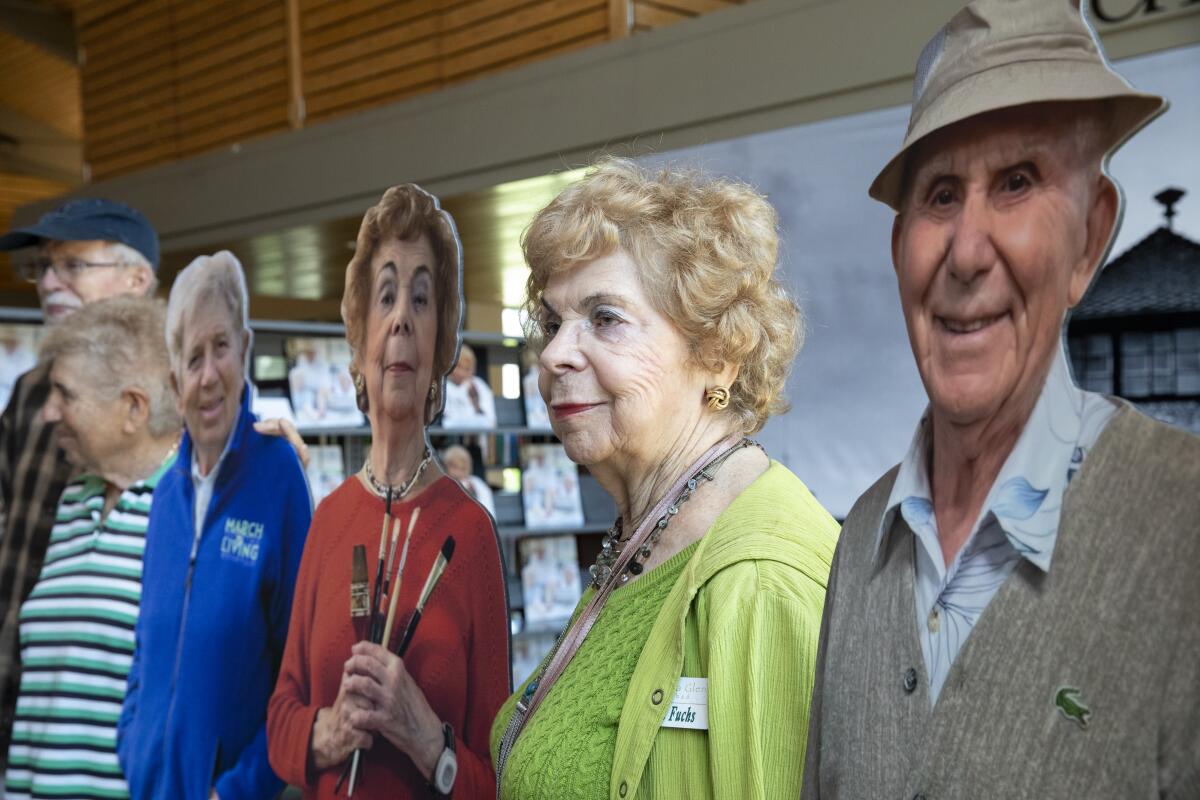 Anita Fuchs stands next to a cardboard cutout of herself at a Holocaust remembrance exhibit at Rancho San Diego Library