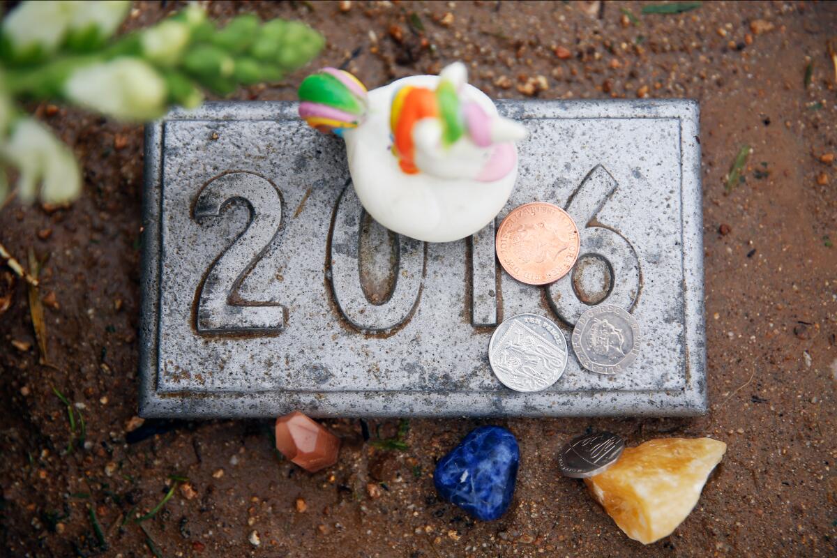 A grave marker with the year 2016, with mementos and coins placed on and around it.
