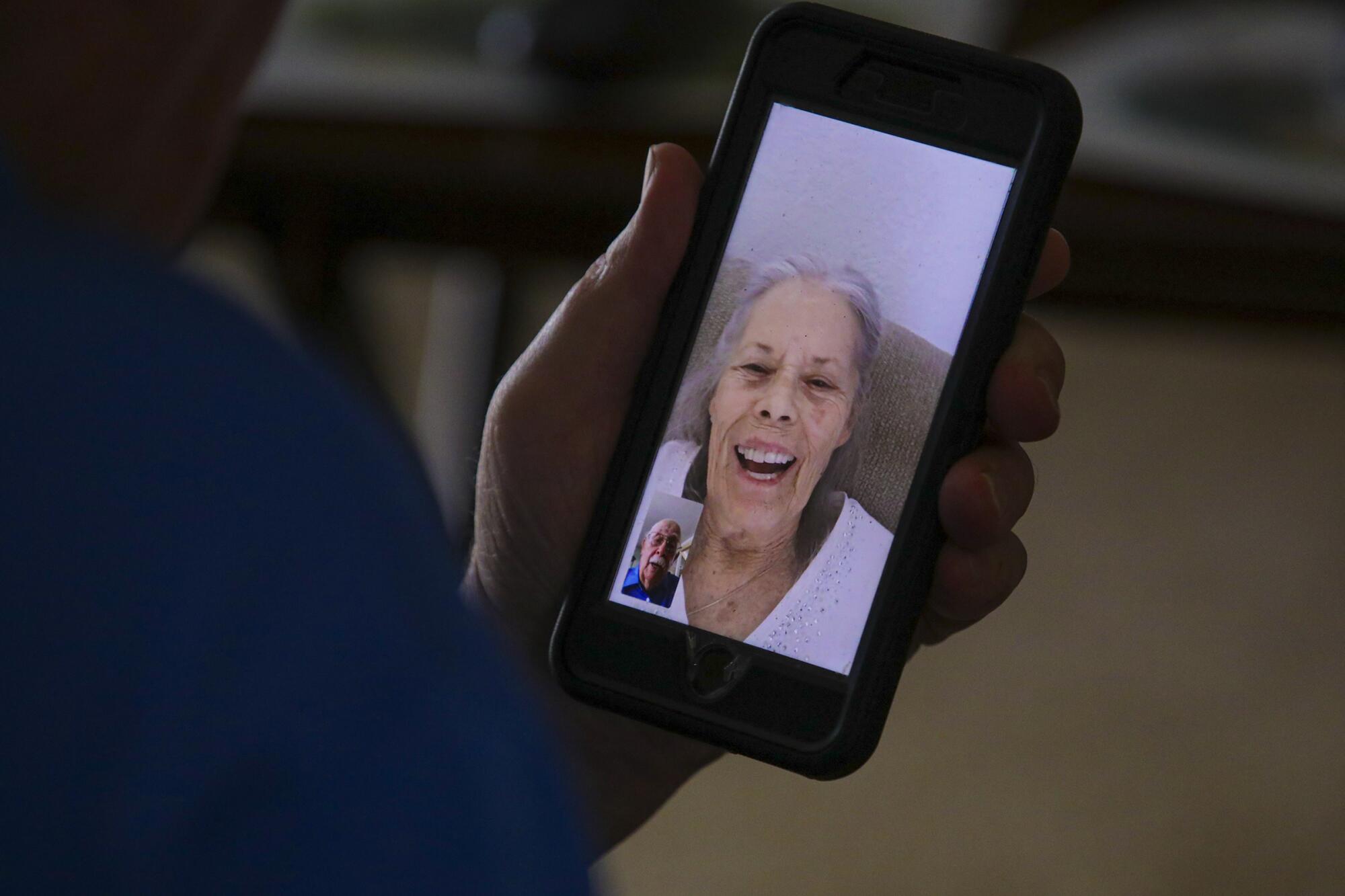 An elderly woman on the screen of a phone held by her husband during a video call
