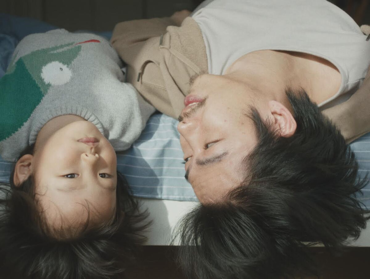 A young boy and a man lay side by side on their backs on a bed in the anthology the "The Year of the everlasting Storm.