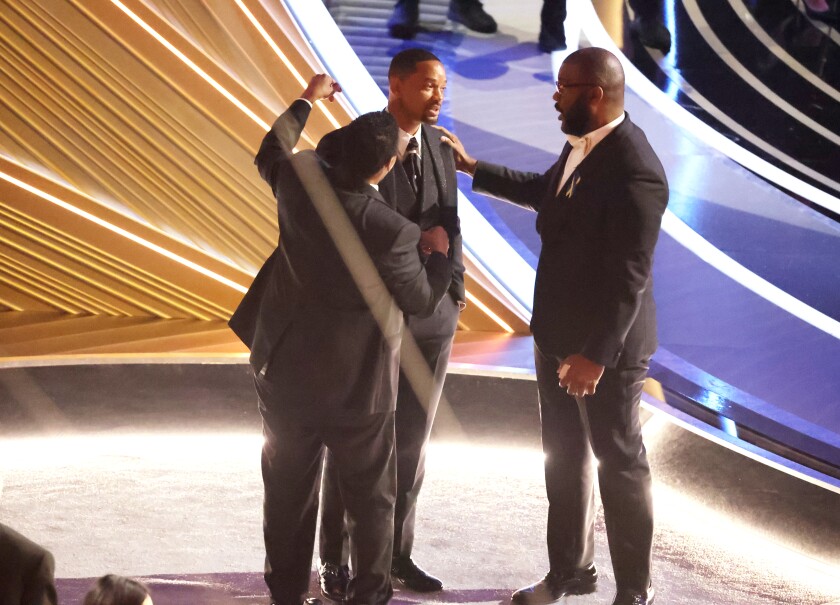 Three men stand near the Oscars stage.