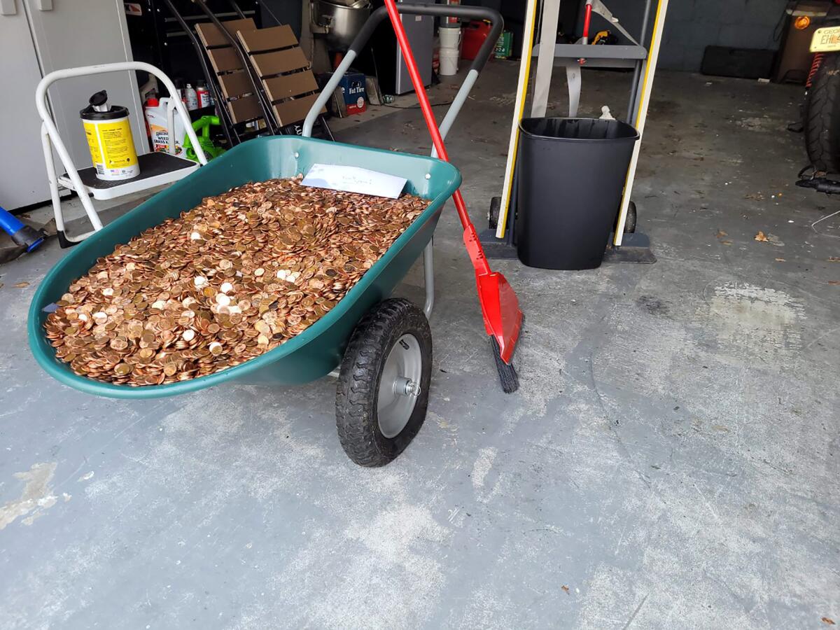 This image provided by Olivia Oxley shows a wheelbarrow filled with pennies, March 20, 2021 in Fayetteville, Ga. A Georgia man said his former employer owed him a pretty penny, $915 to be exact, after leaving his job in November. But Andreas Flaten said he was shocked to see his final payment: 90,000 oil or grease covered pennies, at the end of his driveway earlier this month, news outlets reported. Atop the pile was an envelope with Flaten's final paystub and an explicit parting message. (Olivia Oxley via AP)