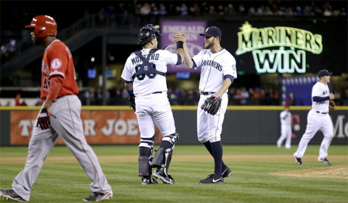 Howie Kenrick walks off the field as closer Tom Wilhelmsen and catcher Jesus Montero celebrate the Mariners' win over the Angels, 3-2.
