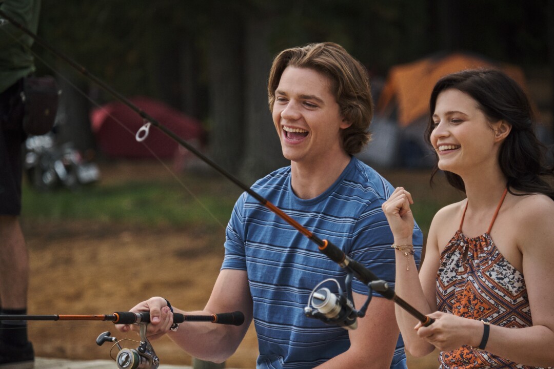 A teenage boy and girl hold fishing rods and laugh