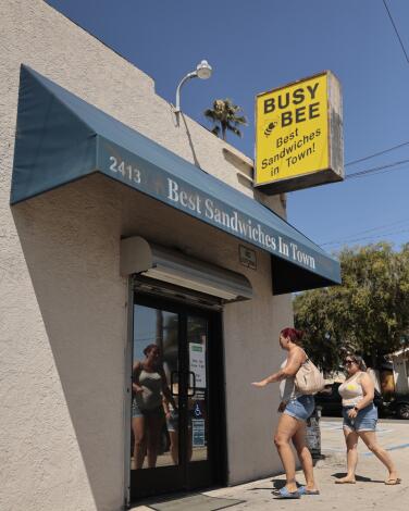 Patrons enter the Busy Bee Market, with a sign that says "best sandwiches in town" above the door.