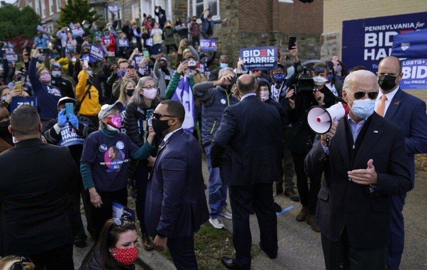 Joe Biden in a mask holds a megaphone in front of a group of supporters