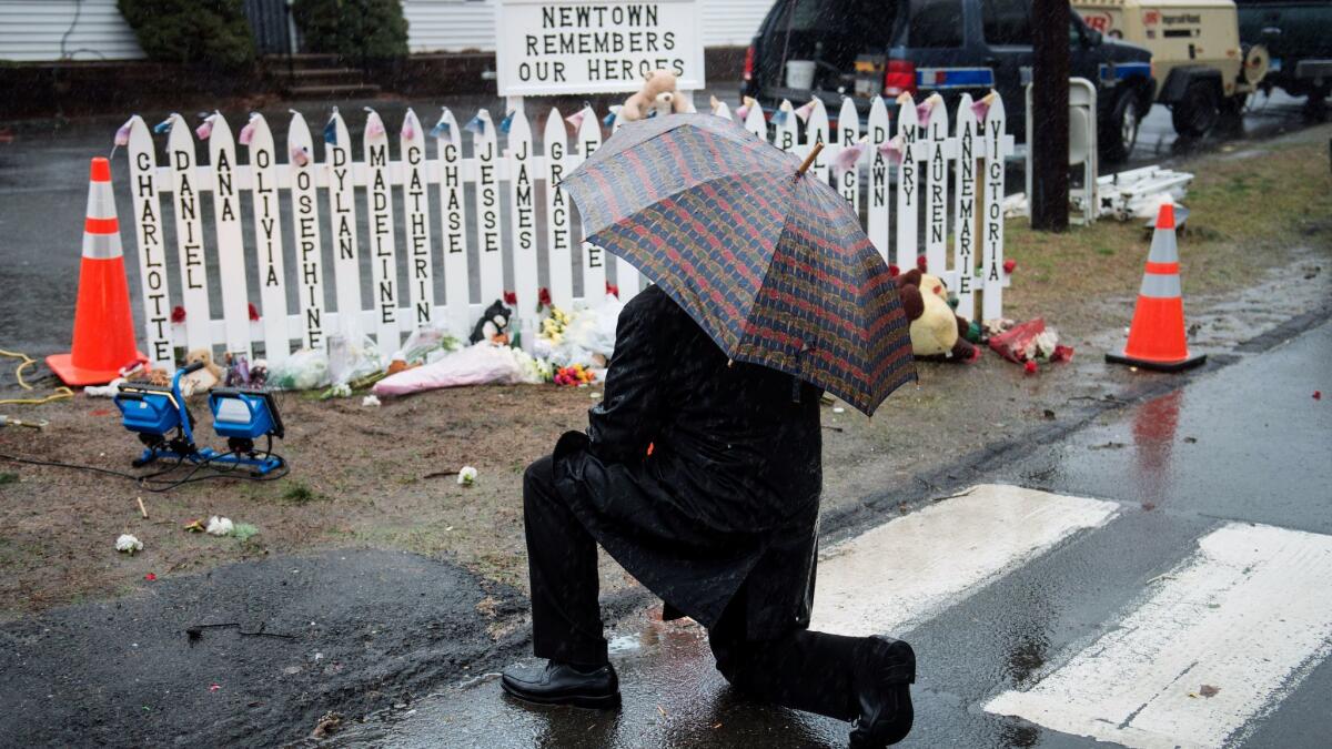 A man kneels at a picket fence with the names of shooting victims during a moment of silence in Sandy Hook village in Newtown, Conn., in 2012.