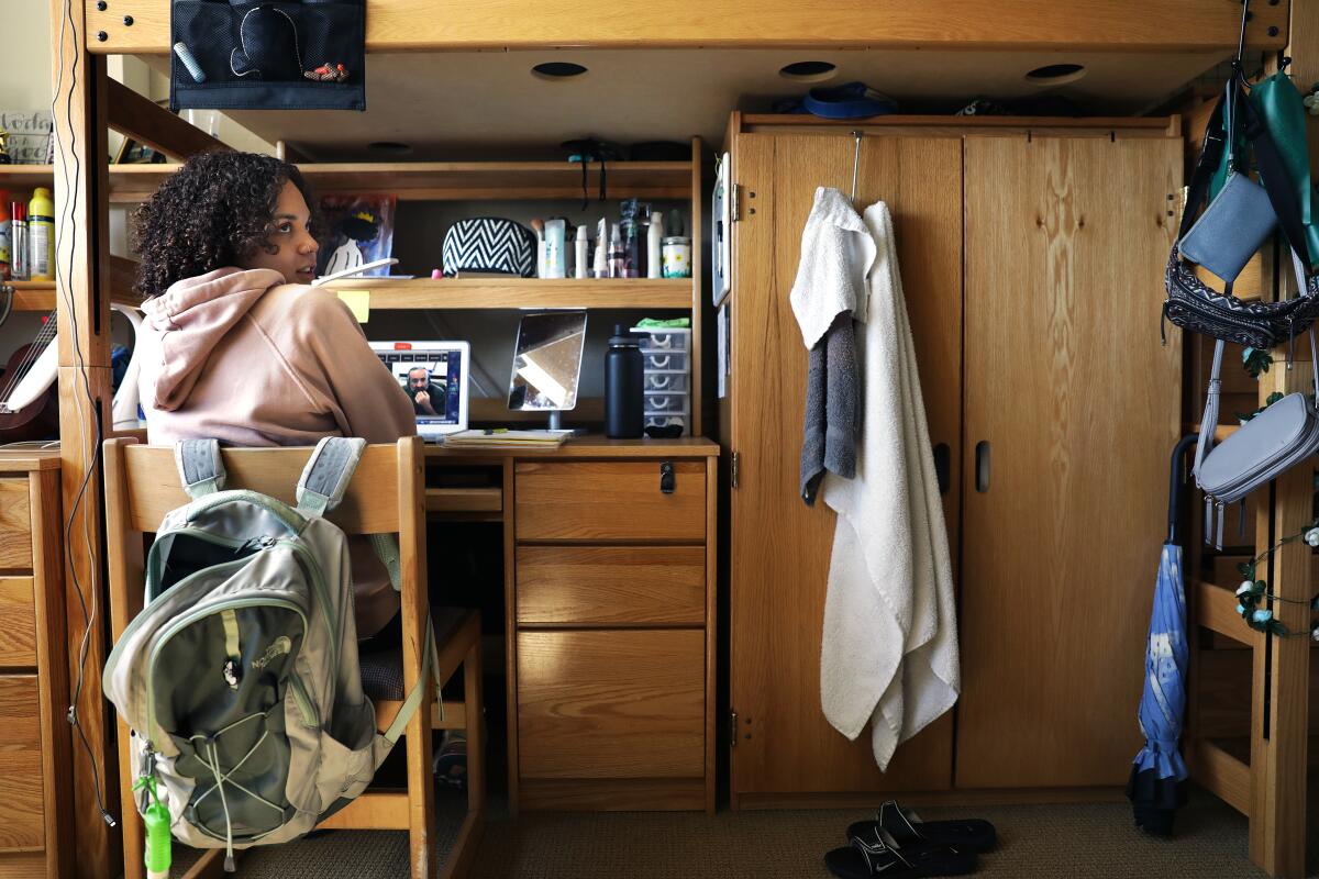A student sits at a desk in a dorm room.