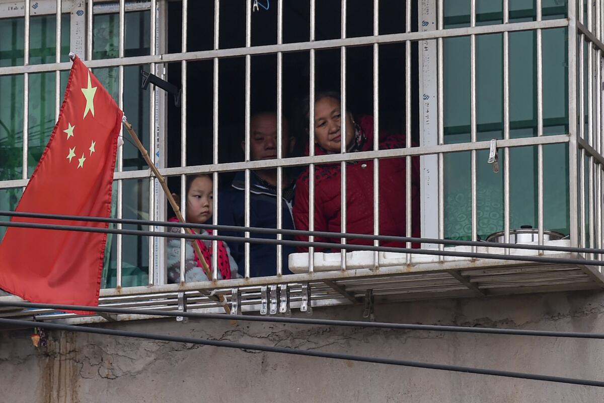 A family looks out the window of their home in a neighborhood on the outskirts of Wuhan. 