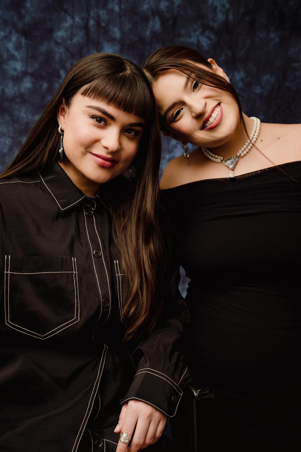Devery Jacobs and Paulina Alexis lean their heads together and smile for a portrait.