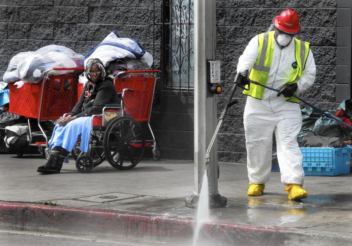 A homeless woman named Patricia watches a sanitation worker from her wheelchair near the corner of 6th Street and Gladys Avenue in downtown L.A.