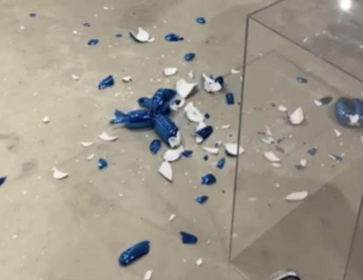 The shattered pieces of a blue porcelain statue lie on the concrete floor at an art fair