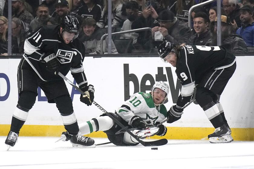 Dallas Stars center Ty Dellandrea, center, falls as he battles for the puck with Los Angeles Kings center Anze Kopitar, left, and right wing Adrian Kempe during the first period of an NHL hockey game Tuesday, Jan. 3, 2023, in Los Angeles. (AP Photo/Mark J. Terrill)