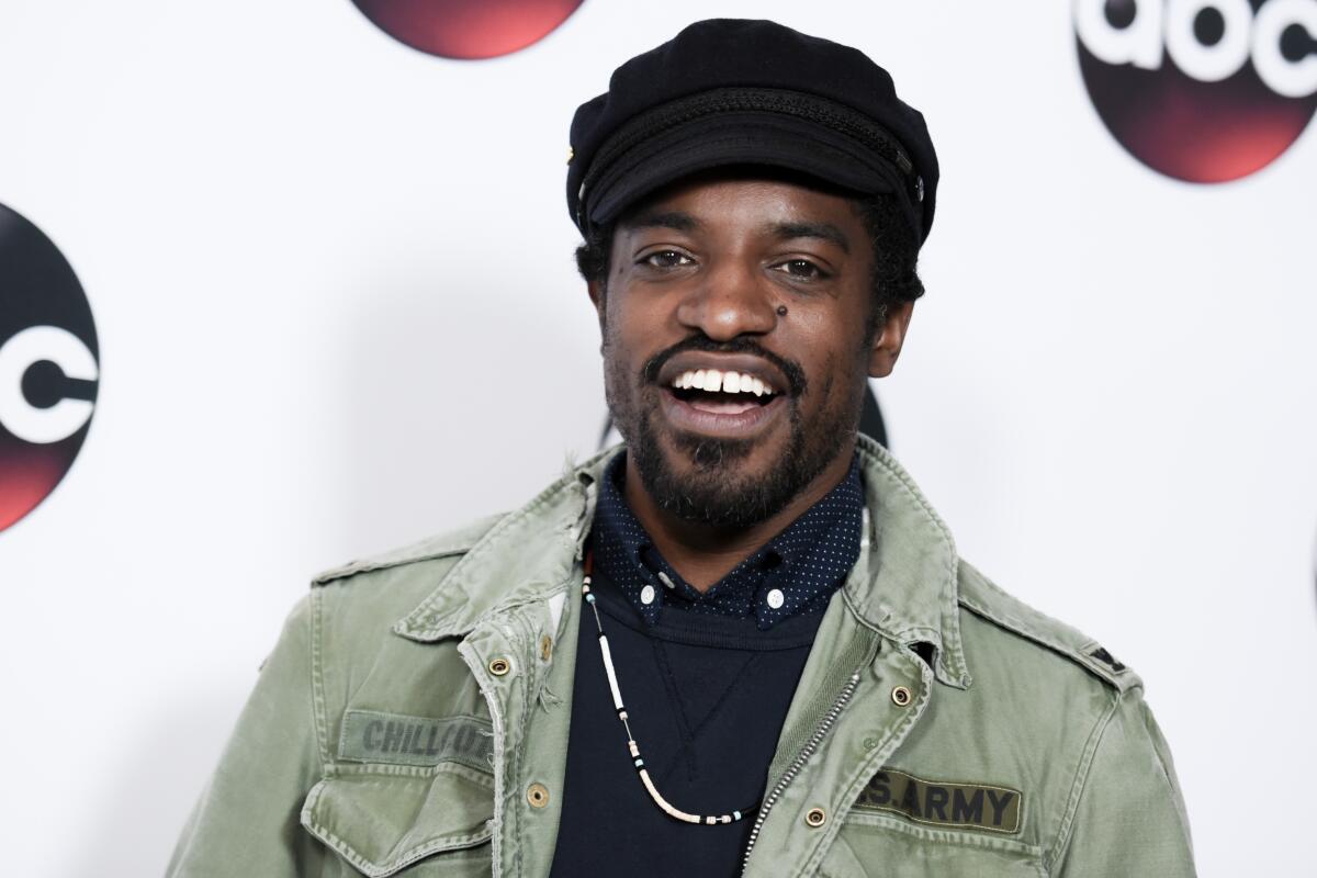 Andre 3000 wearing a newsboy cap, a black shirt and a military-style jacket