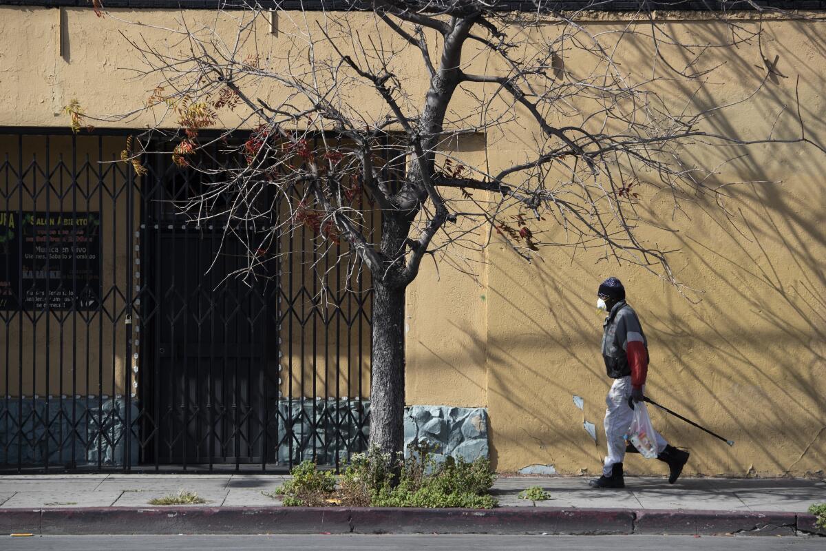 A man carries groceries past the shuttered Beylul Restaurant on Saturday, April 4, 2020 in West Adams, CA.
